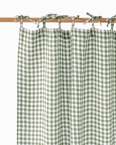 a green and white checkered curtain hanging from a wooden rod with two clips on it