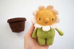 a hand holding a small crocheted doll next to a brown and white cup