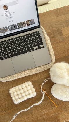 an open laptop computer sitting on top of a wooden table next to yarn and knitting needles