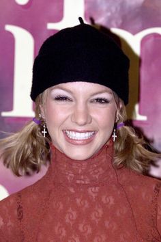 a woman with blonde hair wearing a red dress and black beanie smiles at the camera