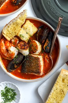 there is a bowl of seafood and mussels on the table next to bread