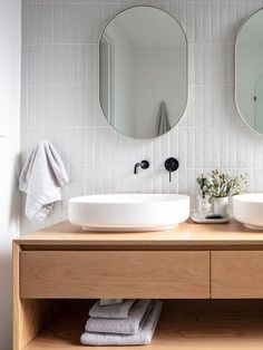 two round mirrors on the wall in a bathroom with wooden cabinets and white tile walls