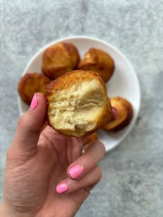 a hand holding a half eaten doughnut in front of a bowl of donuts