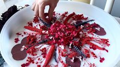 a white plate topped with lots of red flowers next to a person's hand