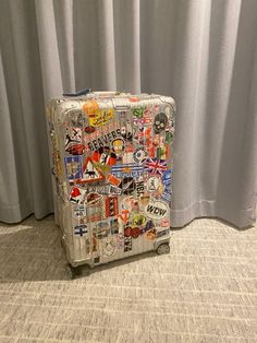 a piece of luggage with stickers all over it sitting on the floor next to a curtain