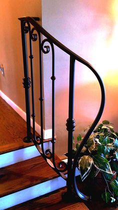 an iron stair rail next to a potted plant on the side of a wooden staircase