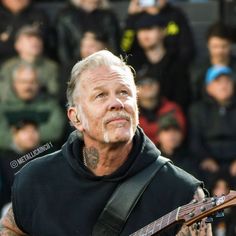 an older man with tattoos playing a guitar in front of a large group of people