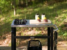 an outdoor grill with two bottles on it and a bag sitting next to the grill