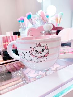 a cup with a cat on it sitting on top of a counter next to makeup brushes