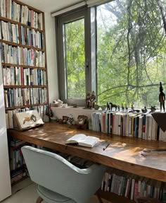 a desk with books on it in front of a large window and lots of bookshelves