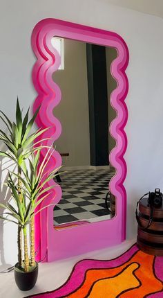 a pink mirror sitting on top of a white table next to a potted plant