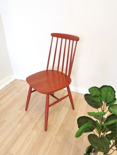 a red chair sitting on top of a hard wood floor next to a potted plant