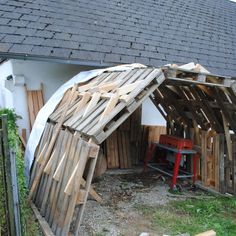 a small shed made out of pallets and wooden planks with a red chair in the corner