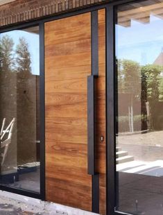 a wooden door with black frame and glass on the side of a brick building in front of trees