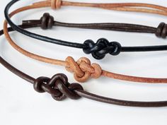 three different colored leather bracelets on a white surface with black and brown cords attached to them