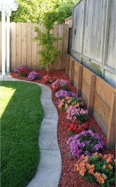 a flower bed in the middle of a yard with flowers growing on it and a wooden fence