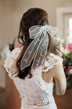 the back of a woman's head wearing a wedding dress with a ribbon on it