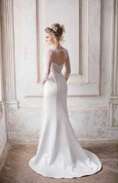 a woman in a white wedding dress standing against a wall with her back to the camera