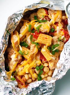 a foil wrapper filled with chicken, beans and cheese covered in seasoning next to a fork