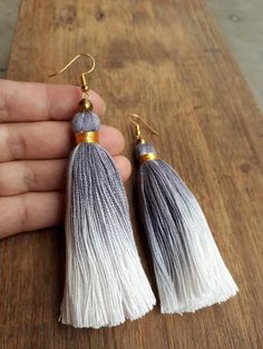 the tasseled earrings are made from white and grey yarn, with gold accents