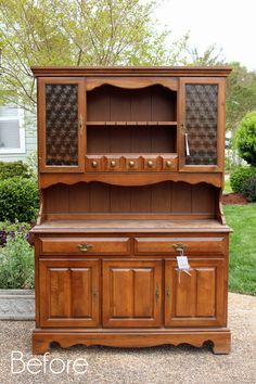 an old wooden china cabinet with glass doors on the top and bottom, in front of a house