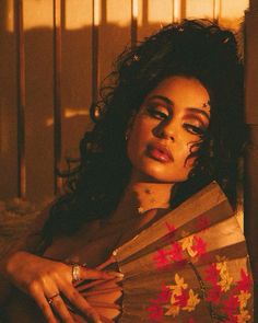 a woman with makeup on her face holding a fan and looking off to the side