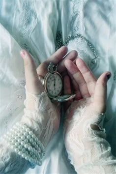 a person holding an old pocket watch in their hands with pearls on the wrist and white gloves