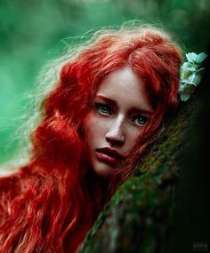 a woman with long red hair leaning against a tree