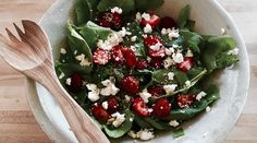 a salad with strawberries and feta cheese in a bowl next to a wooden spoon