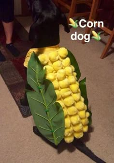 a dog standing next to a fake corn on the cob costume made out of leaves