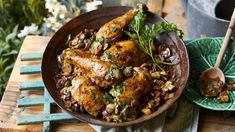 a wooden table topped with a bowl filled with chicken and beans next to a green plate