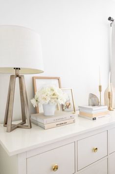 a white dresser topped with books and flowers