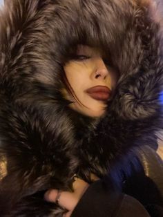 a woman wearing a fur coat and hood with her eyes closed while she is looking at the camera