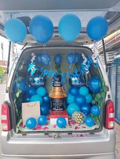 the back end of a silver van filled with blue balloons and gifts for someone's birthday