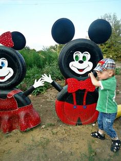 a young boy standing next to two large mickey mouses on top of a dirt field