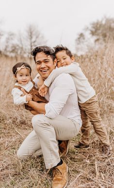 a man holding two children in his arms and smiling at the camera while standing in a field