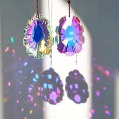 two colorful earrings hanging from strings on a wall with light shining through the window behind them