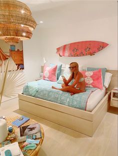 a woman sitting on top of a bed next to a surfboard hanging from the ceiling