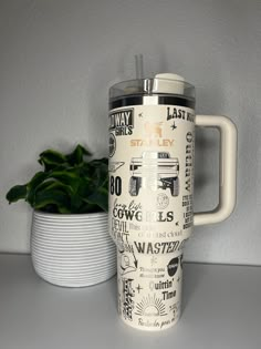 a white coffee mug sitting on top of a table next to a potted plant