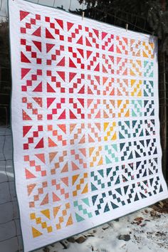 a quilt hanging on a fence in the snow with an orange, yellow and green color scheme