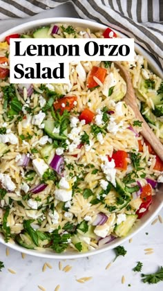 a white bowl filled with pasta salad and topped with feta cheese, tomatoes, cucumbers, red onions and parsley