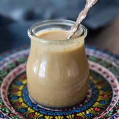 a small glass jar filled with peanut butter on top of a colorful plate and spoon