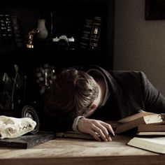 a person laying down on a table with books and a skull in front of them