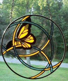 a stained glass sun catcher hanging on a chain in the grass with trees behind it