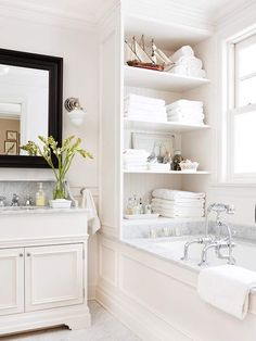 a bath room with a tub a sink and a shelf filled with white folded towels