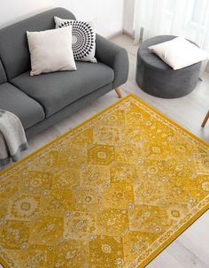 a living room with a gray couch, yellow rug and white pillows on the floor