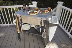 an outdoor grill on a deck with plates of food sitting on the burner area