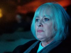 an older woman with blue hair looking off into the distance at night in front of a street light