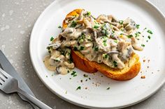 a white plate topped with two pieces of bread covered in mushroom gravy next to a fork