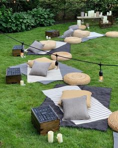 an outdoor seating area with pillows and lights on the grass, surrounded by candles in front of trees